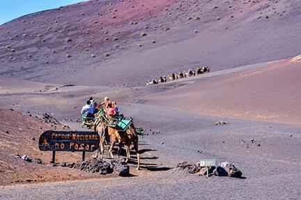 Turistas montados en dromedario junto al cartel de Parque Natural de Timanfaya